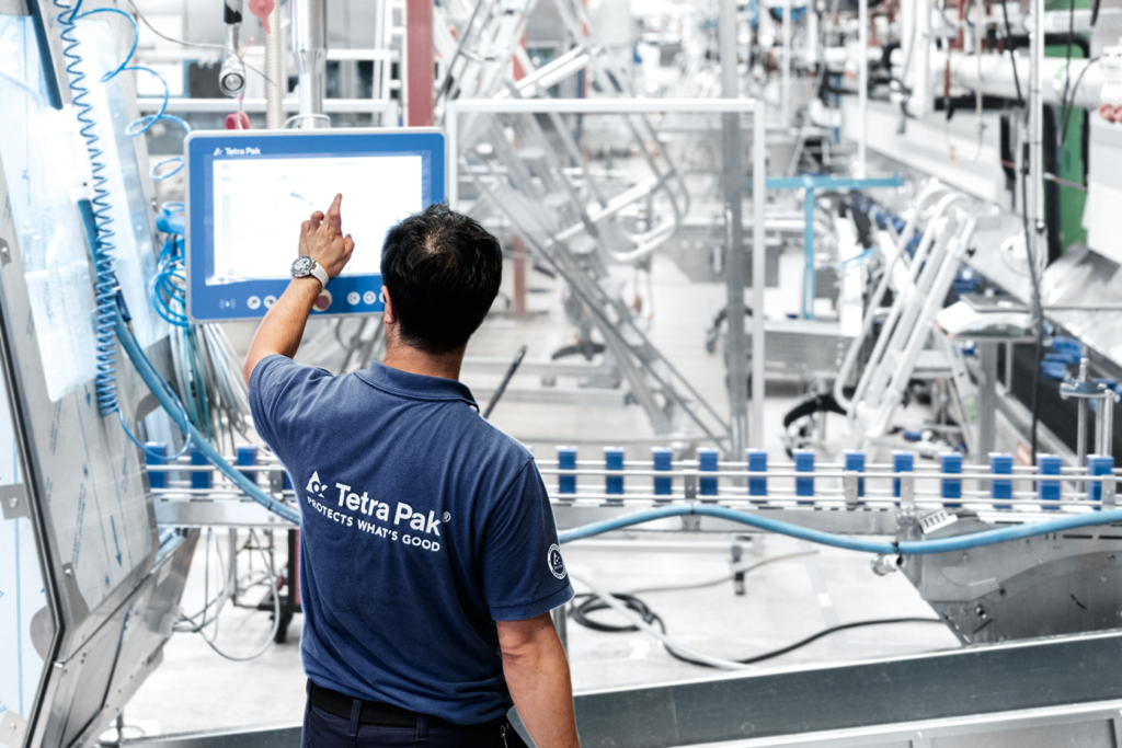 A male engineer adjusting settings on a screen for a conveyer belt in a Tetra Pak plant.
